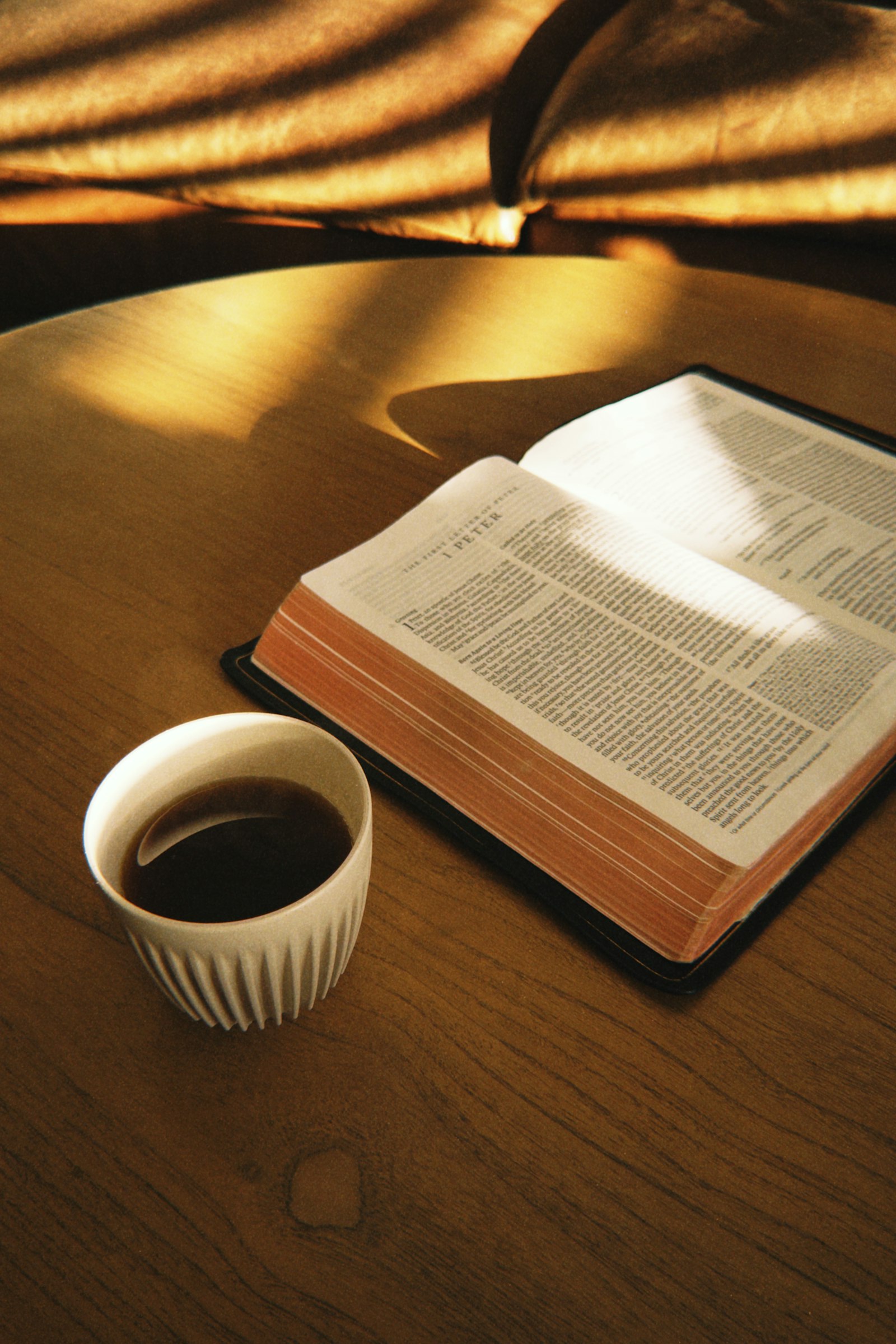 An open Bible beside a cup of coffee in warm sunlight